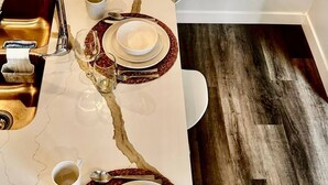 A dining table set with plates, bowls, glasses, and cutlery, with a modern kitchen sink and a light fixture above. - Brighton Escape, Spacious 2BR Walk-out Suite (Saskatoon)