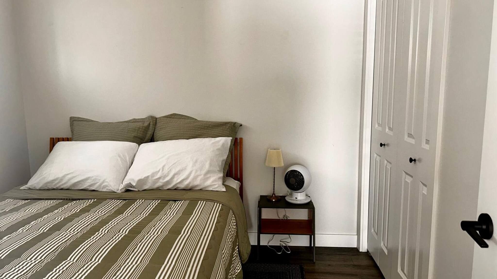 Un dormitorio con cama, almohadas, una mesita de noche con lámpara y una puerta.