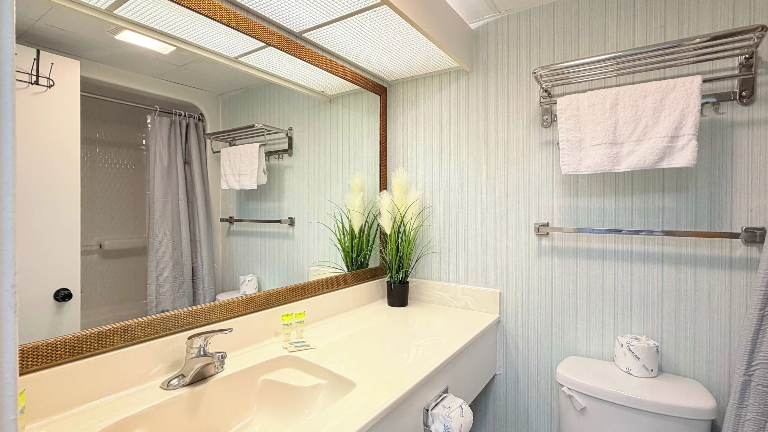 A bathroom with a large mirror, a sink, a toilet, and a shower area.