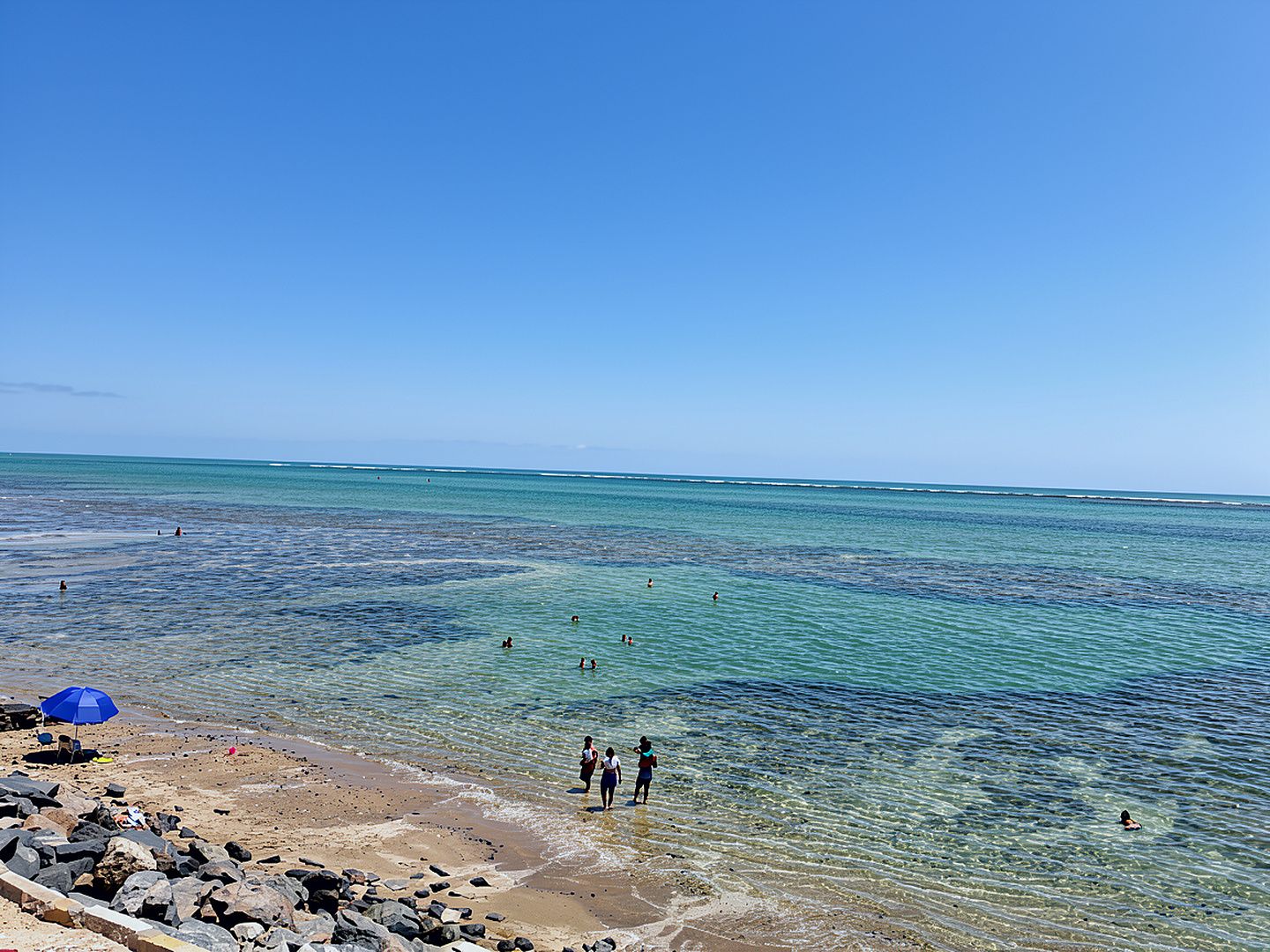 Una playa con agua cristalina, rocas y algunas personas.