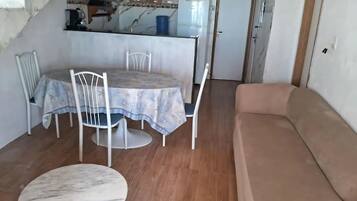 En stue med et rundt marmorbord, en beige sofa og et spiseområde med bord og stole.