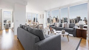 A modern living room with a grey sofa, a coffee table, and a view of a cityscape through large windows.