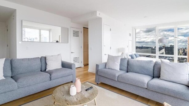 A modern living room with two grey sofas, a round coffee table, and a large window offering a city view.