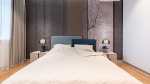 A neatly made bed with a headboard, two bedside lamps, a wall-mounted air conditioner, and a window with curtains. - Playwright Test Hotel 1789175829844 (Seattle)