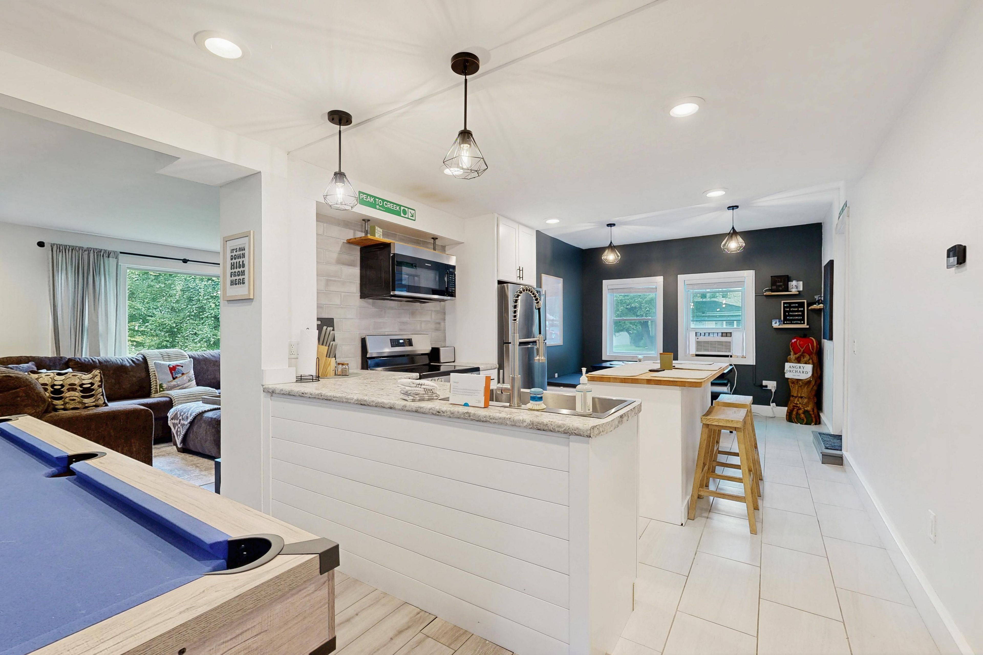A modern kitchen with a central island, overhead pendant lighting, and a view into the living area.