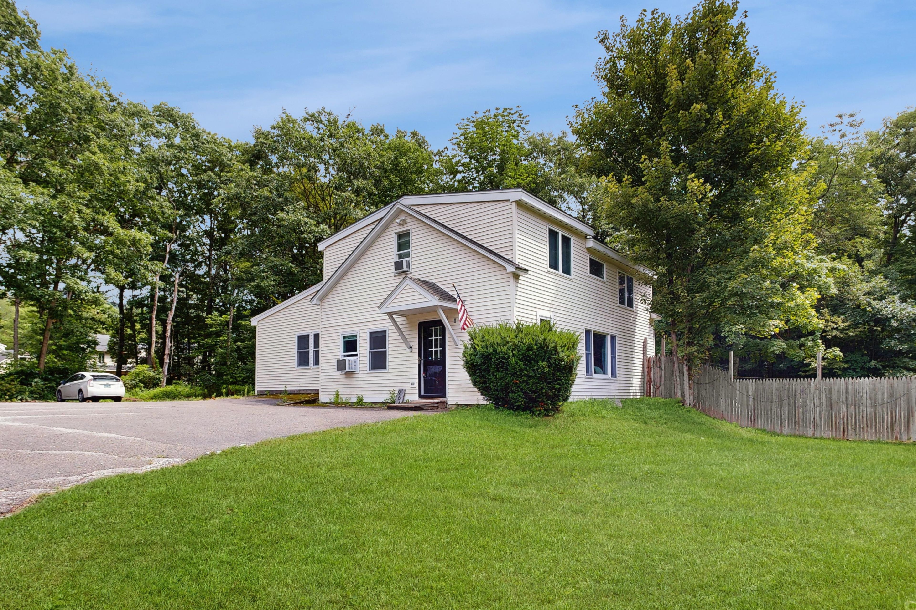 A two-story house with a front porch, a small front yard, and a wooden fence.