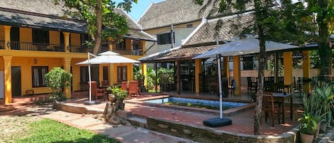 Ein Innenhof mit Sitzgelegenheiten im Freien, einem Pool und einem überdachten Bereich mit Sonnenschirmen.