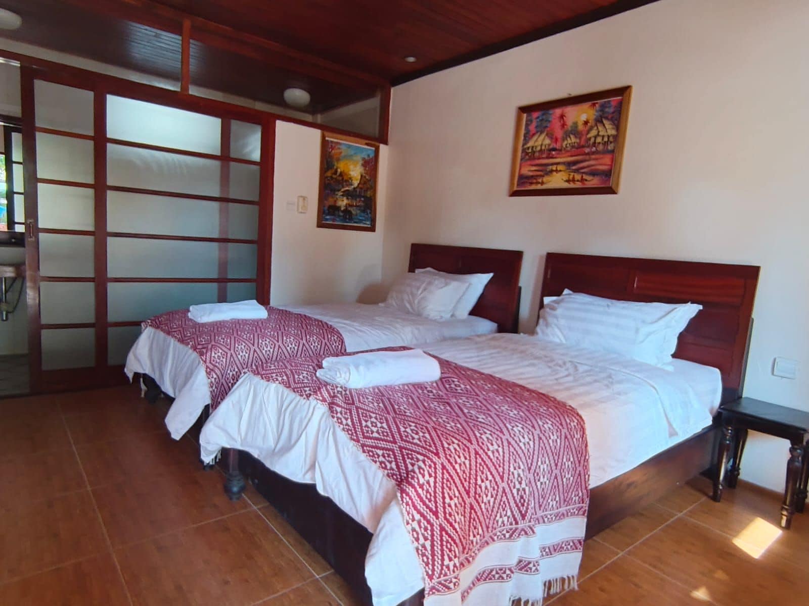 A hotel room with two beds, a wooden headboard, a tiled floor, and a painting on the wall.