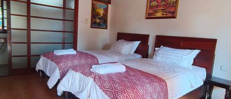Habitación de hotel con dos camas, cabecero de madera, suelo de baldosas y un cuadro en la pared.