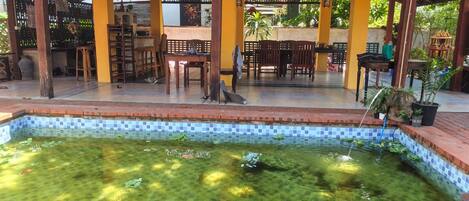 A covered outdoor seating area with a pool and tiled flooring.
