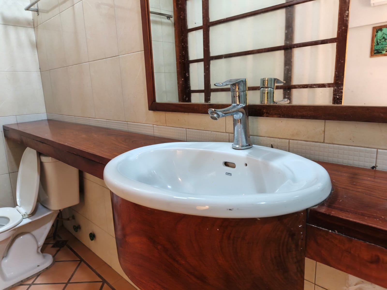 A bathroom with a white sink, a wooden vanity, a toilet, and a mirror with a wooden frame.