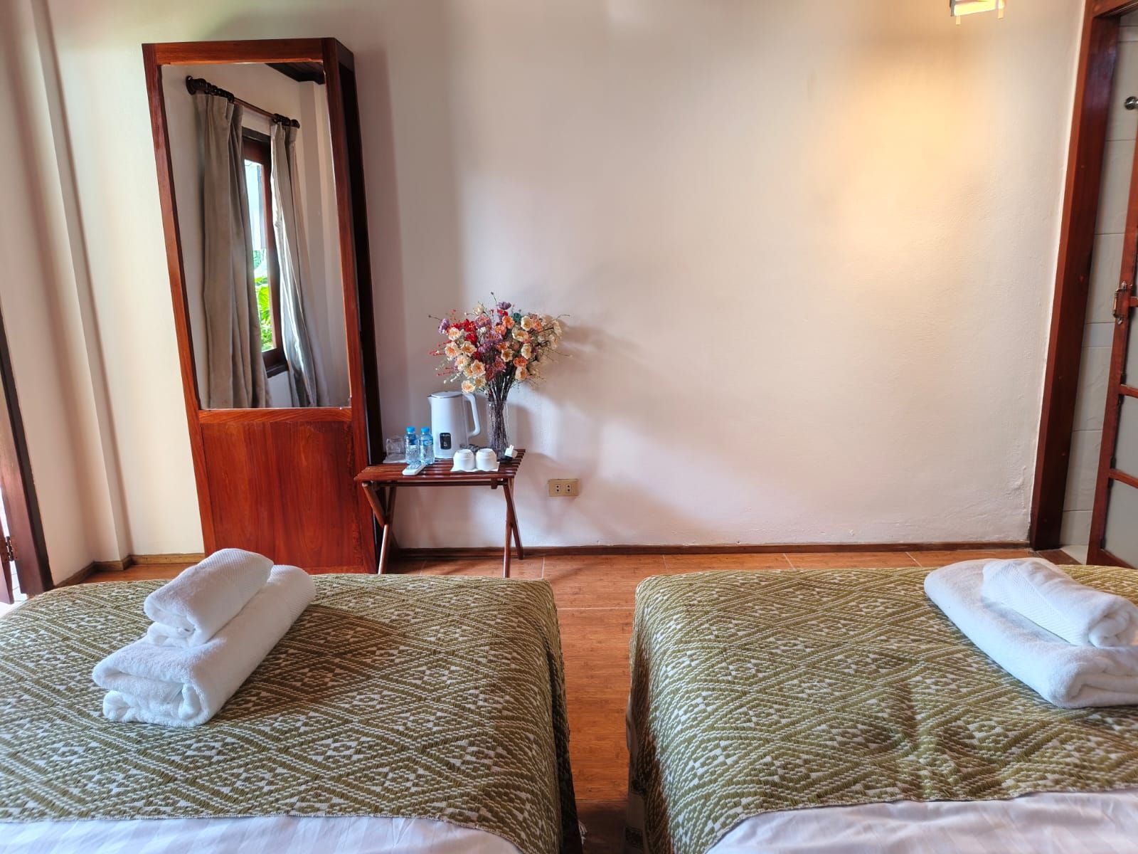 A hotel room with two beds, a small table with a vase of flowers, and a mirror.