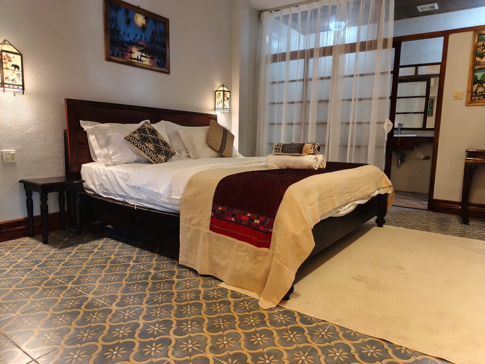 A neatly made bed with a patterned bedspread, a bedside table, and a wall-mounted lamp.