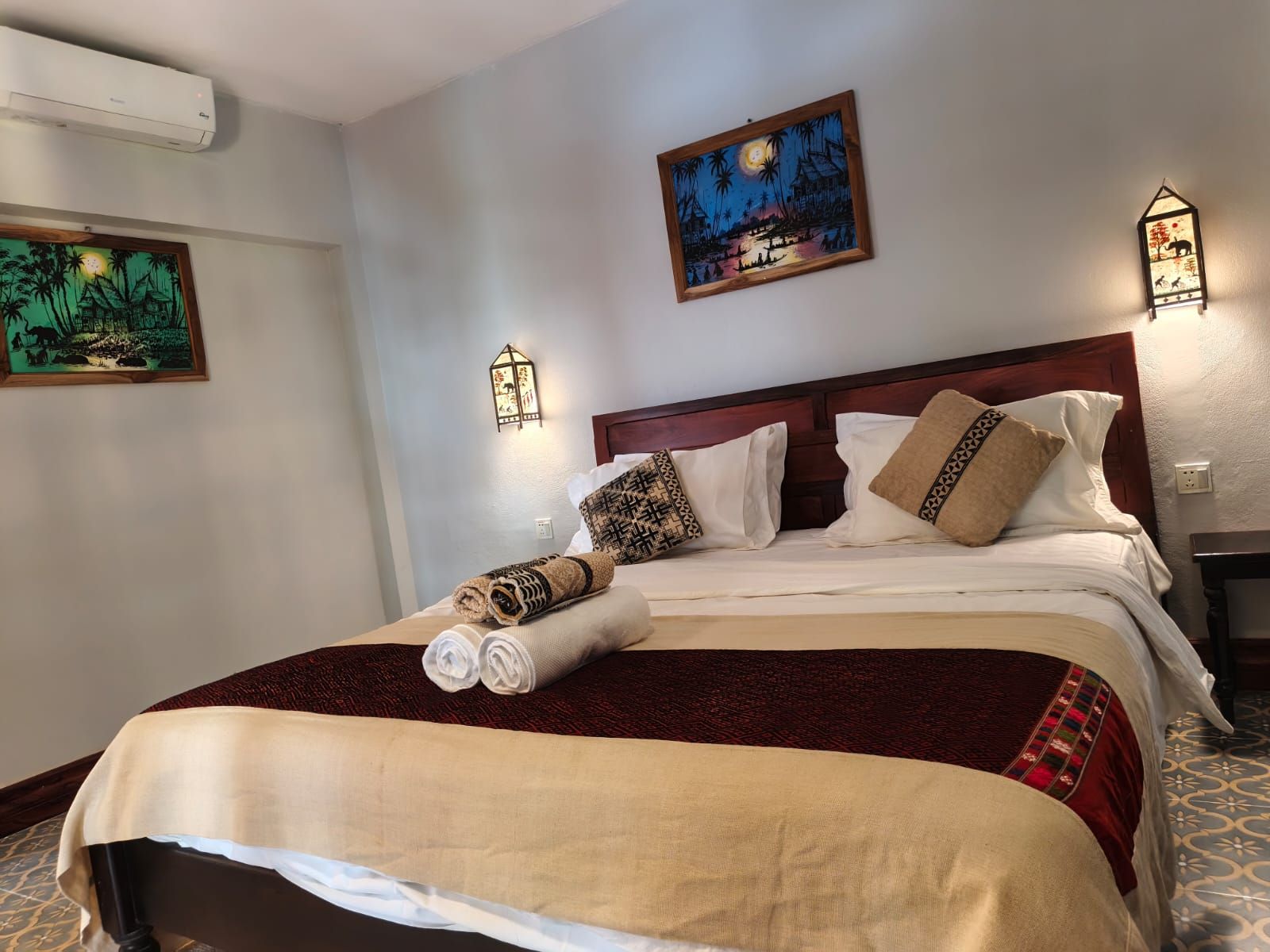 A hotel room with a bed, a nightstand, a wall-mounted air conditioner, and two wall-mounted light fixtures.