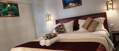 A hotel room with a bed, a nightstand, a wall-mounted air conditioner, and two wall-mounted light fixtures.