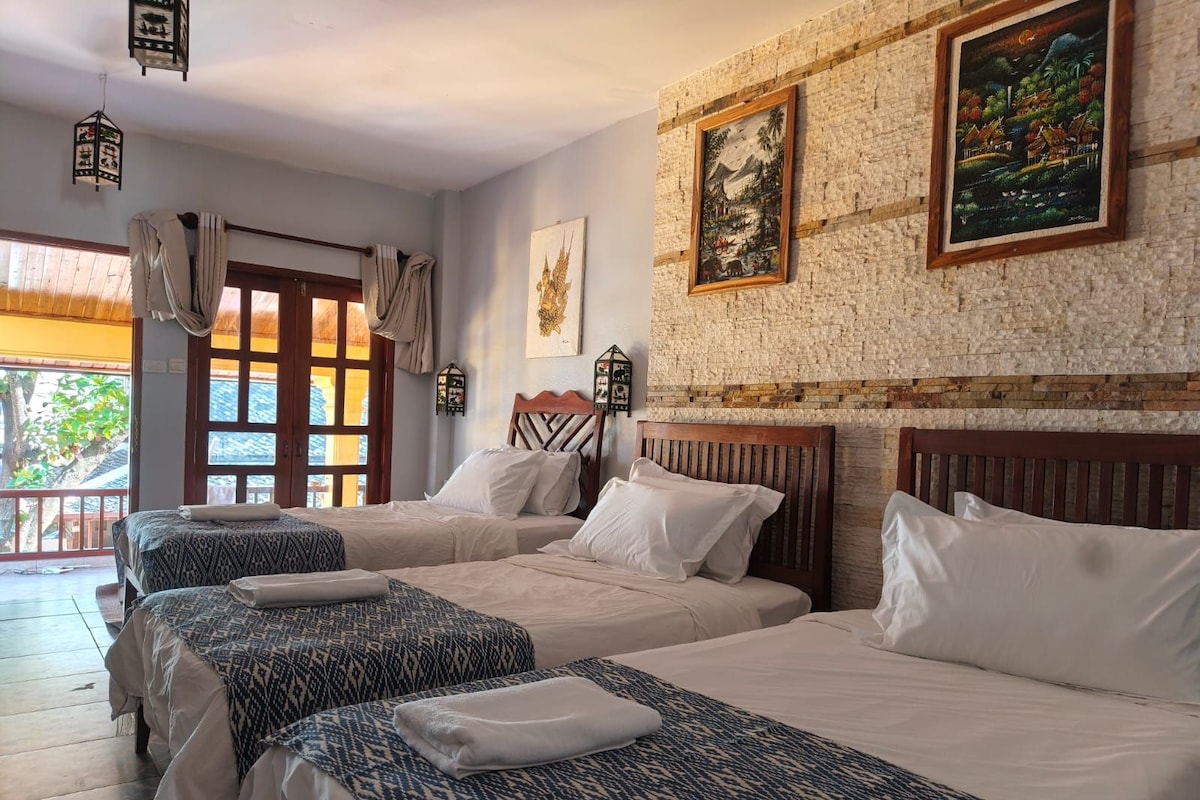 Une chambre d’hôtel avec trois lits, un balcon et un mur en briques orné d’œuvres d’art.