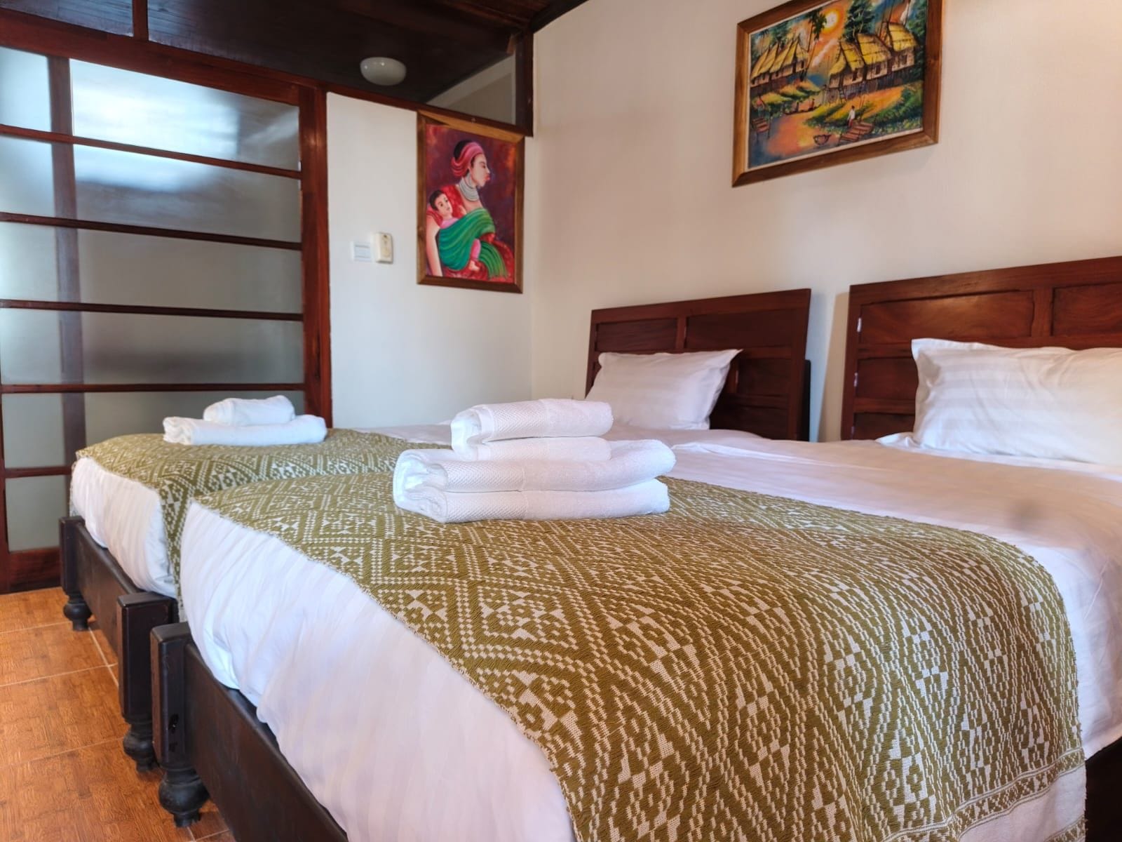 A hotel room with two beds, a wooden headboard, a patterned bedspread, and a painting on the wall.