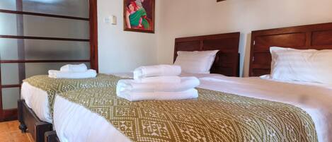 A hotel room with two beds, a wooden headboard, a patterned bedspread, and a painting on the wall.