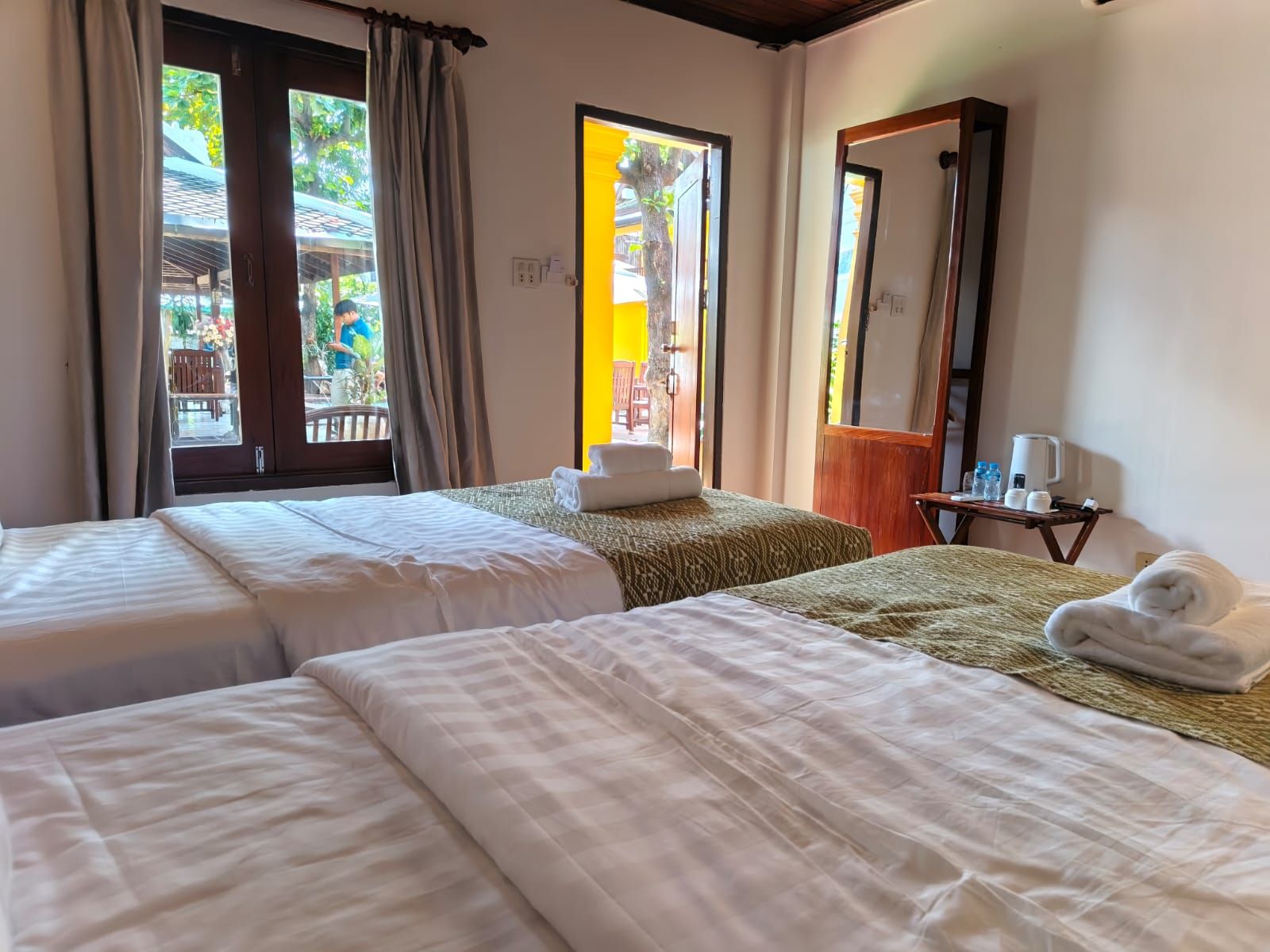 A hotel room with two beds, a bathroom mirror, and a view of the outside.