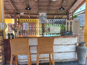 Zona de bar con dos sillones de mimbre, una barra con un ordenador y una pared decorativa con un calendario.