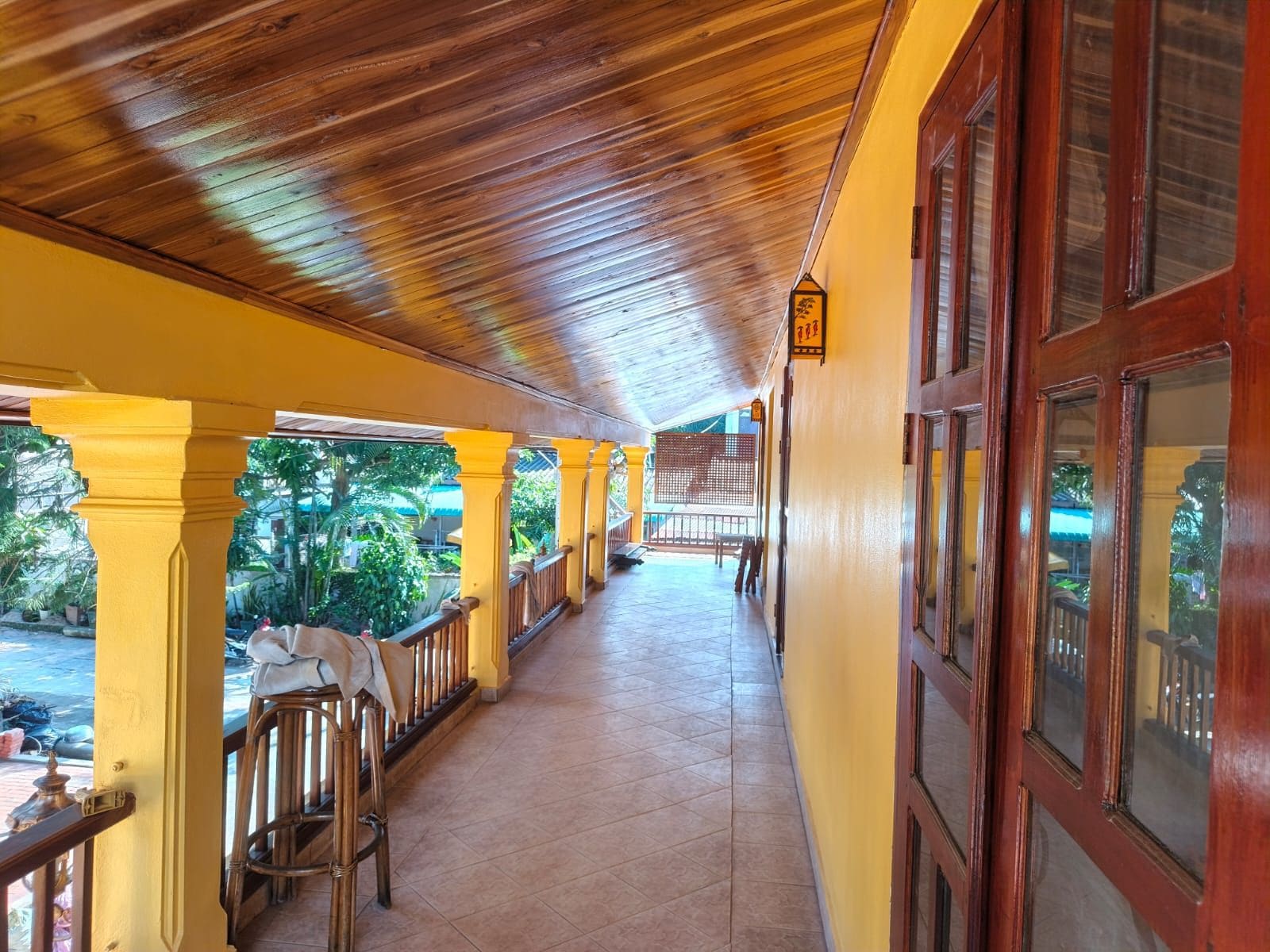 A covered corridor with wooden ceiling and yellow walls, leading to a door with windows.