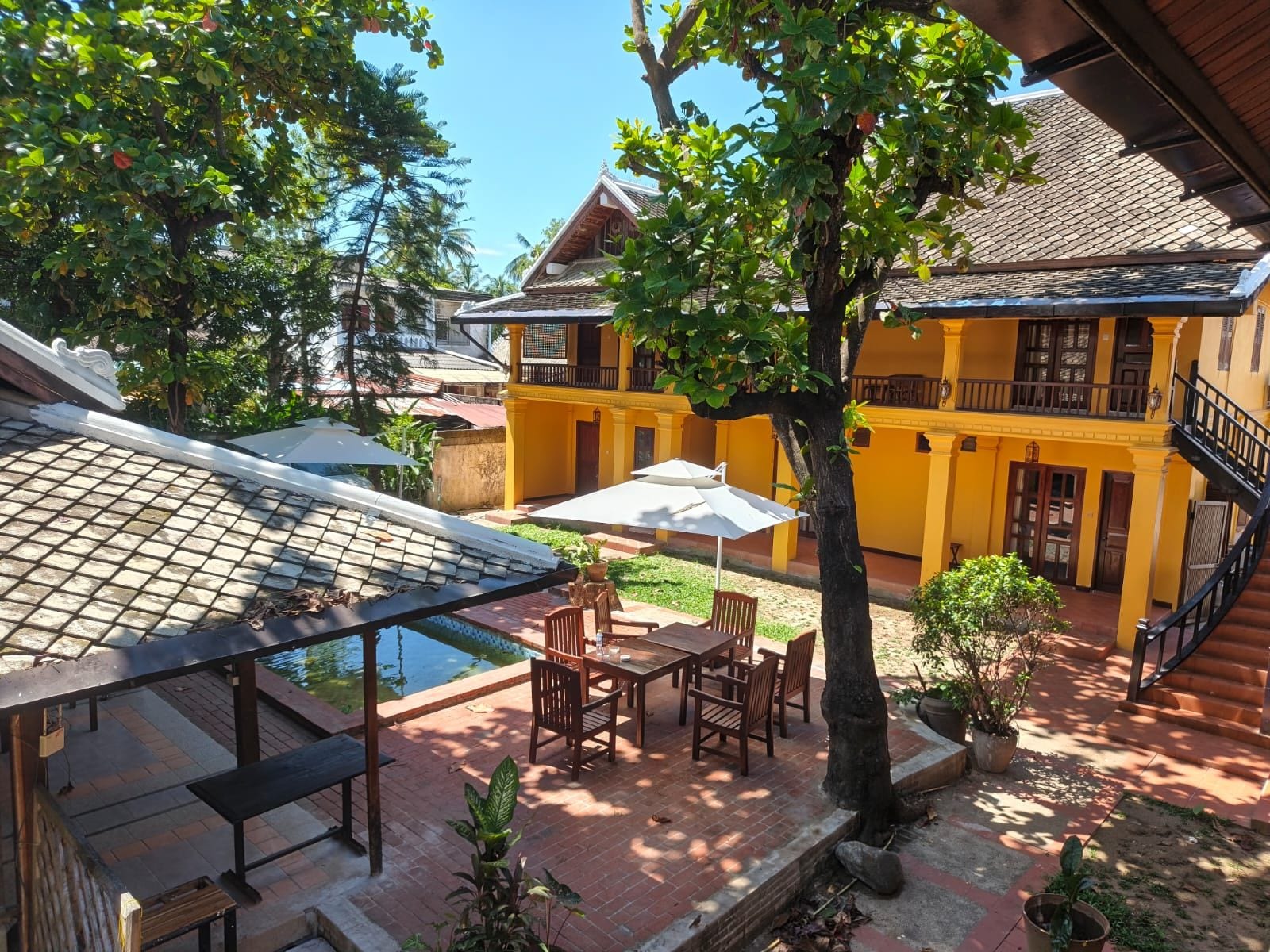 Un patio con piscina, asientos exteriores y un edificio amarillo con balcón.