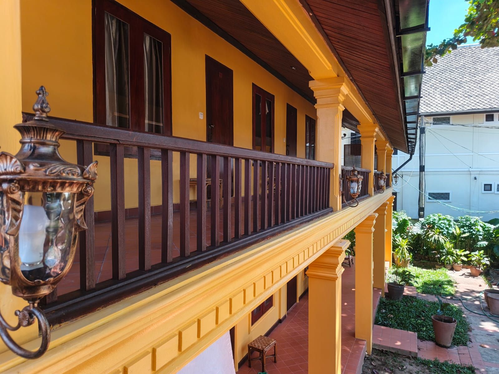 Ein gelbes Gebäude mit Balkon, Blumentöpfen und einer Pflasterterrasse.