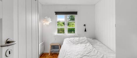 Ein Schlafzimmer mit Bett, einem Fenster mit Blick auf Grünflächen, einem Heizkörper und einer Tür mit Griff.