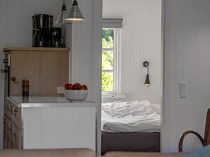 Een kamer met een keukenhoek, een bed en een raam met uitzicht op groen.