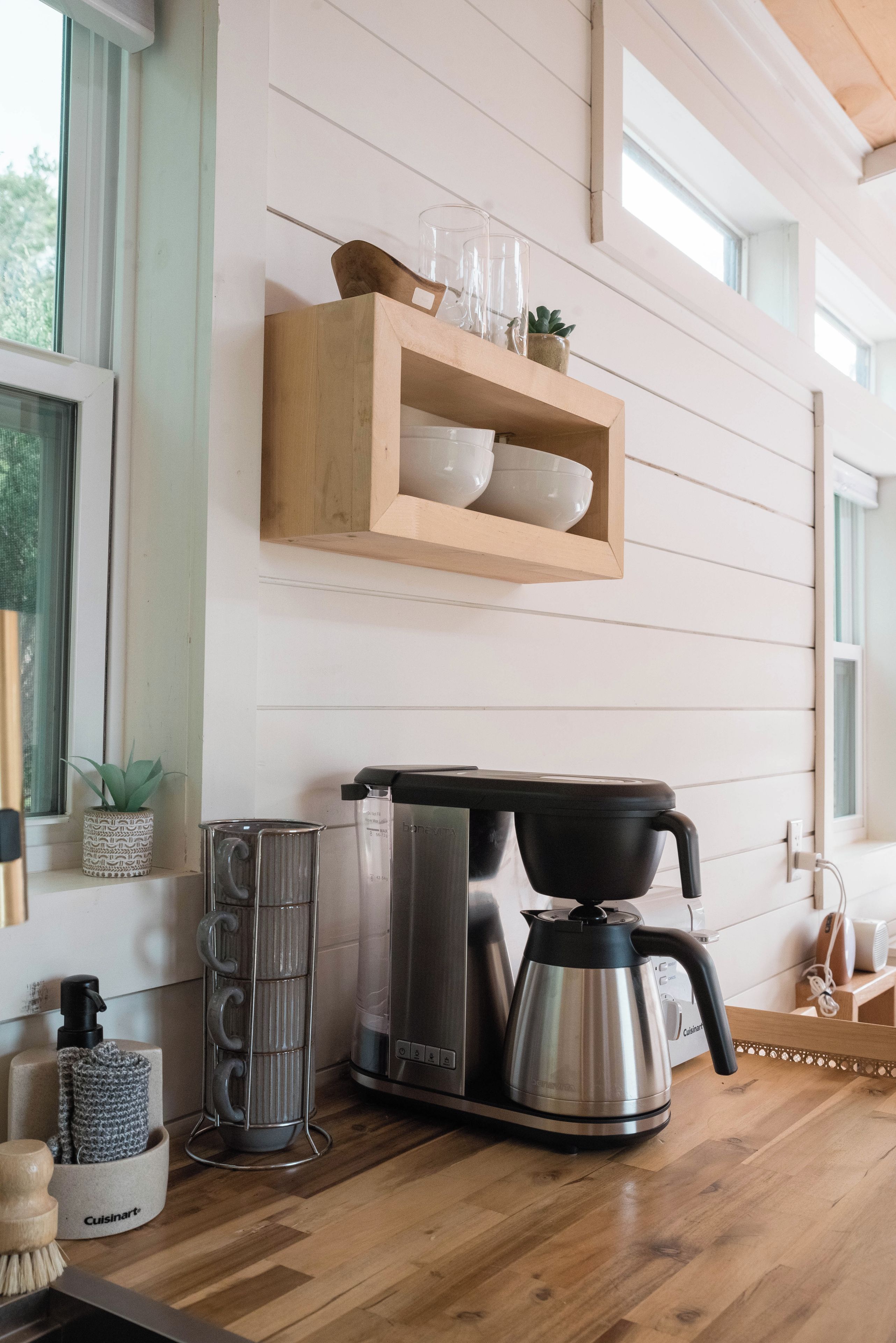 Una cocina con cafetera, hervidor y una repisa con cuencos y vasos.