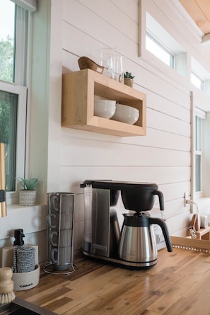 A kitchen with a coffee maker, a kettle, and a shelf with bowls and glasses.