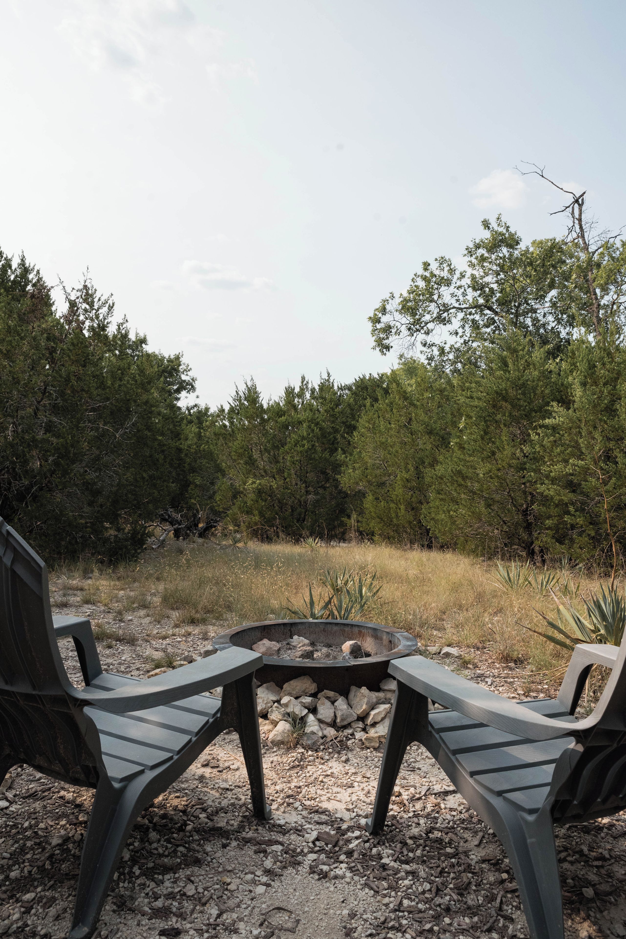 A campsite with two chairs facing a fire pit surrounded by rocks and dry grass.