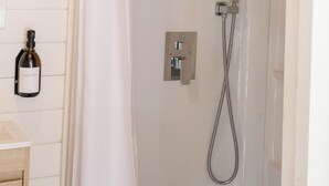 Chuveiro com cortina branca, chuveiro manual e dispensador de sabonete fixado na parede.