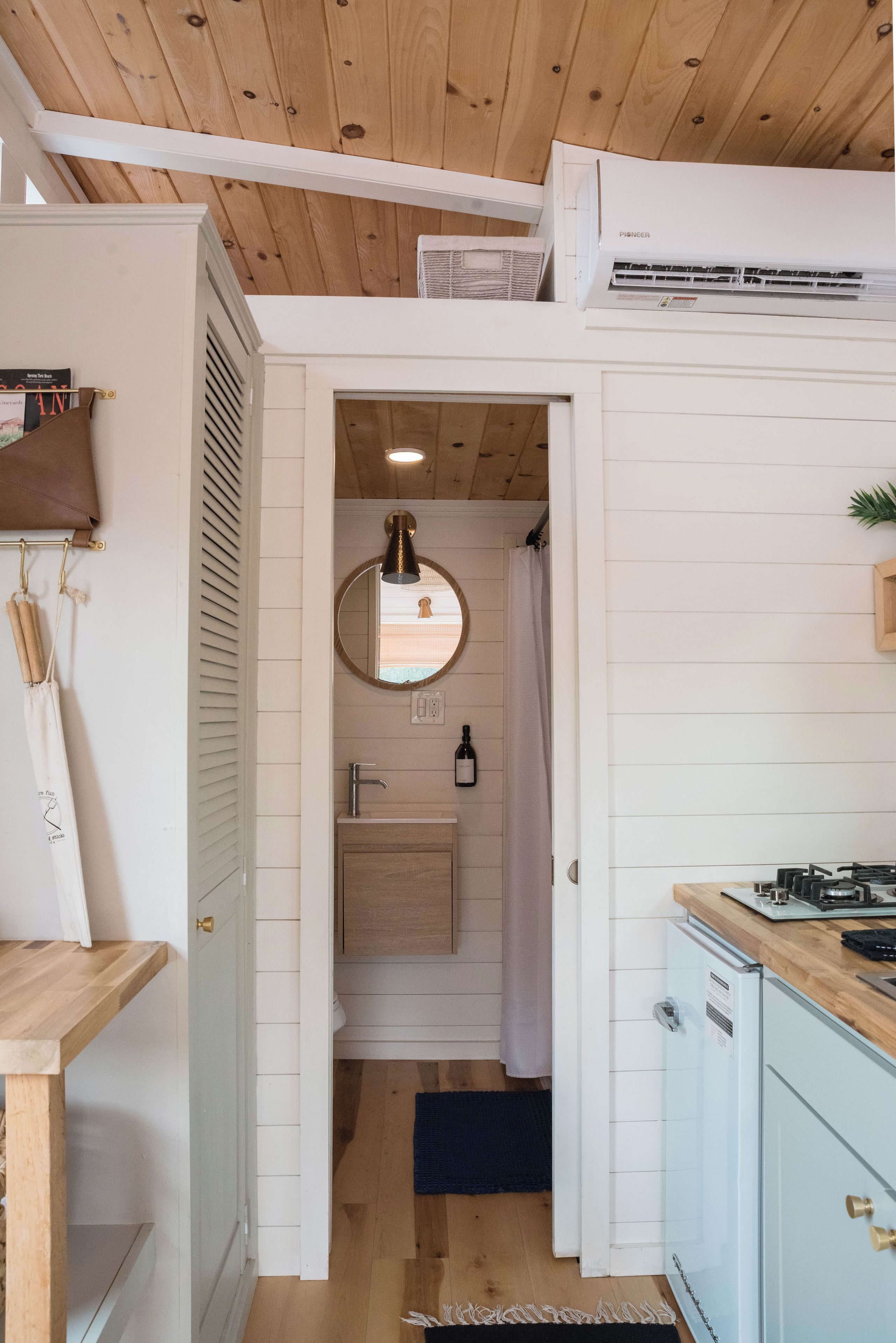 Un pasillo estrecho que conduce a un baño con un espejo redondo, una toalla colgada en la pared y un lavamanos pequeño.