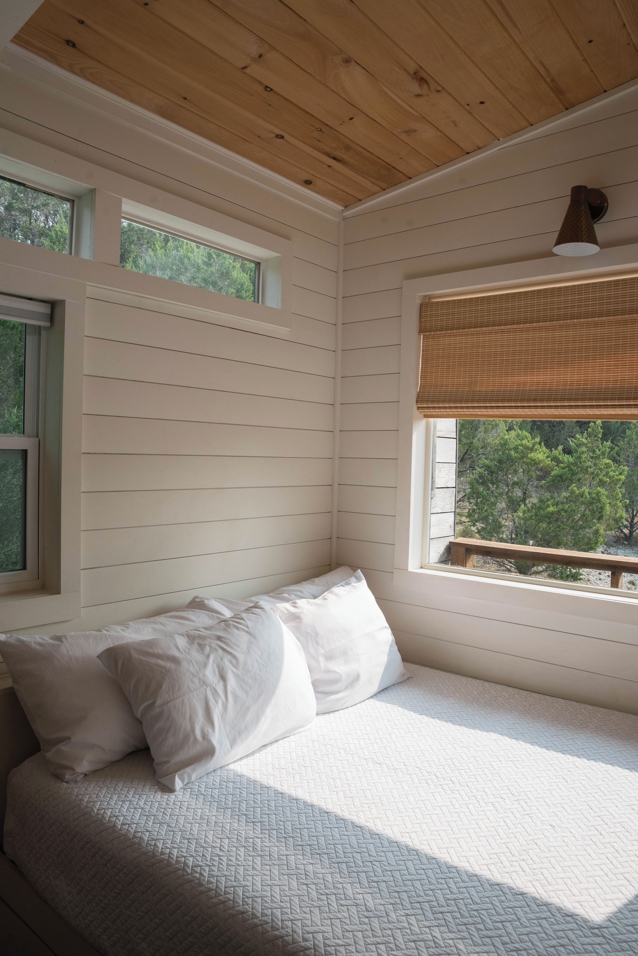 A bedroom with a bed, two windows, and a view of trees.