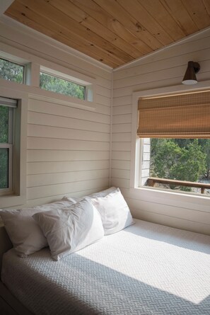 Un dormitorio con una cama, dos ventanas y vistas a árboles.