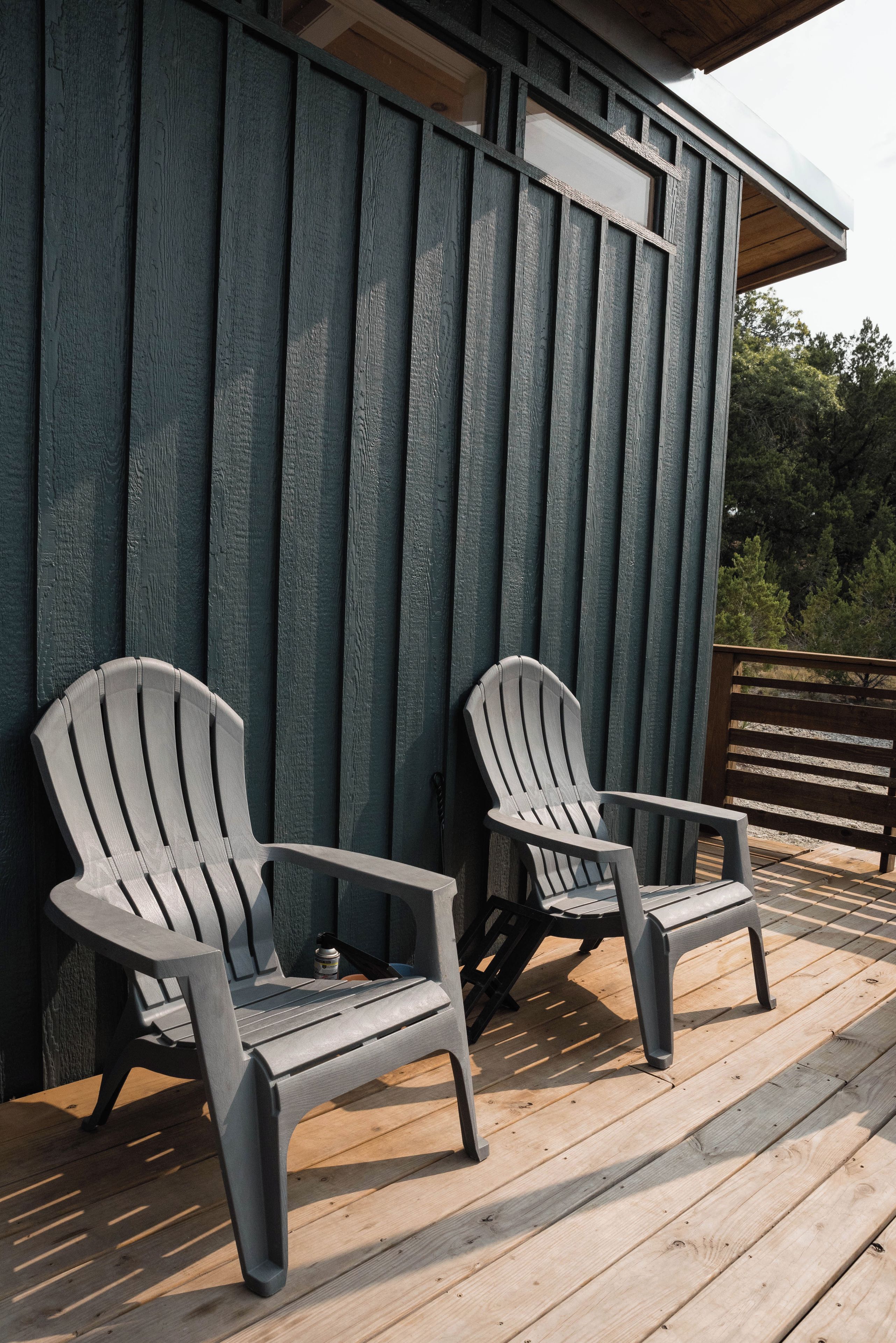 Two Adirondack chairs on a wooden deck with a wooden wall in the background.