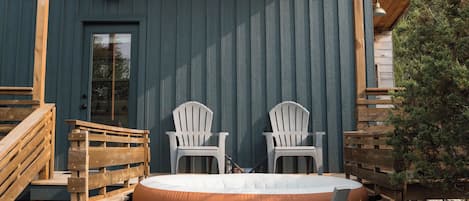 A hot tub with two Adirondack chairs, a wooden deck, and a covered patio area.