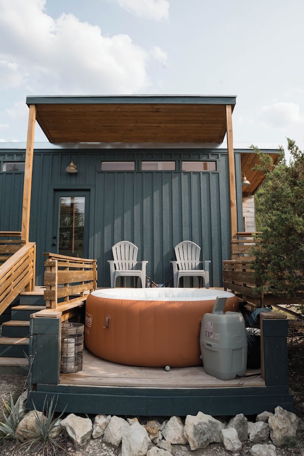 A hot tub with two Adirondack chairs, a wooden deck, and a covered patio area.