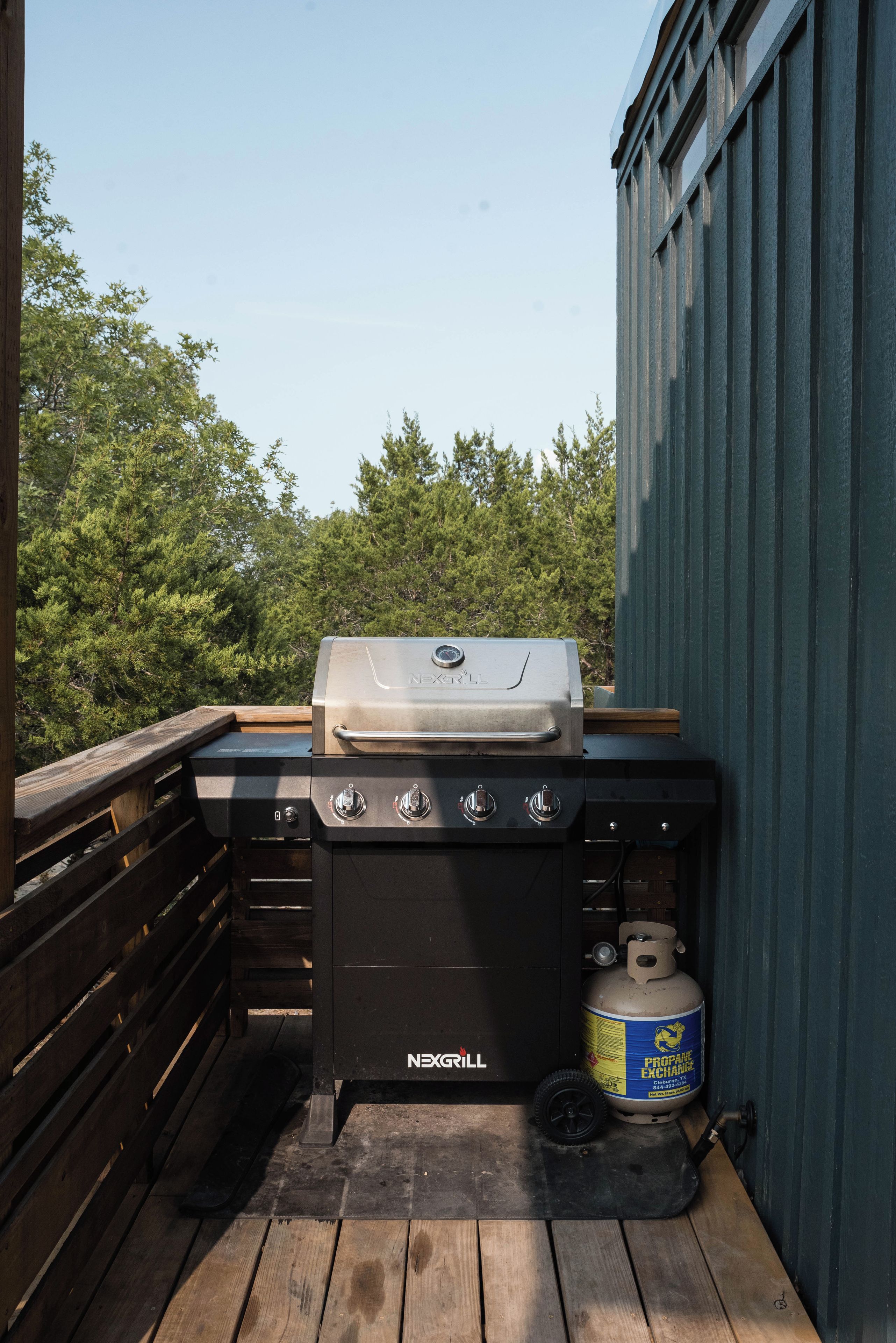 A barbecue grill with a control panel and a propane tank on a wooden deck.