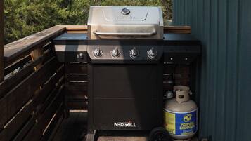 A barbecue grill with a control panel and a propane tank on a wooden deck.