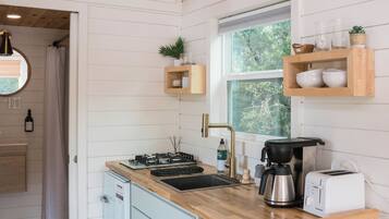 Una cocina moderna con armarios blancos, encimera de madera, estufa integrada y ventana con vistas a zonas verdes.