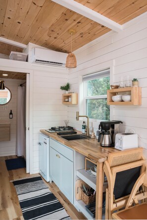 Una cocina moderna con armarios blancos, encimera de madera, estufa integrada y ventana con vistas a zonas verdes.