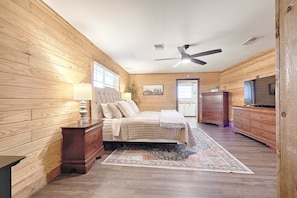 Ein Schlafzimmer mit Holzwänden, einem Bett mit gesteppter Bettdecke, einer Stehlampe, einem Deckenventilator und einer Kommode.