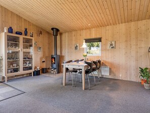 A cozy room with a wooden interior, a table with chairs, a cabinet with glass doors, and a fireplace. - "Fabian" - 300m from the sea by Interhome (Børkop)