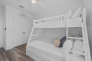 Ein Stockbett mit weißer Bettwäsche und einem Holz-Kopfteil, eine weiße Tür mit einem verzierten Schild und ein Holzboden.
