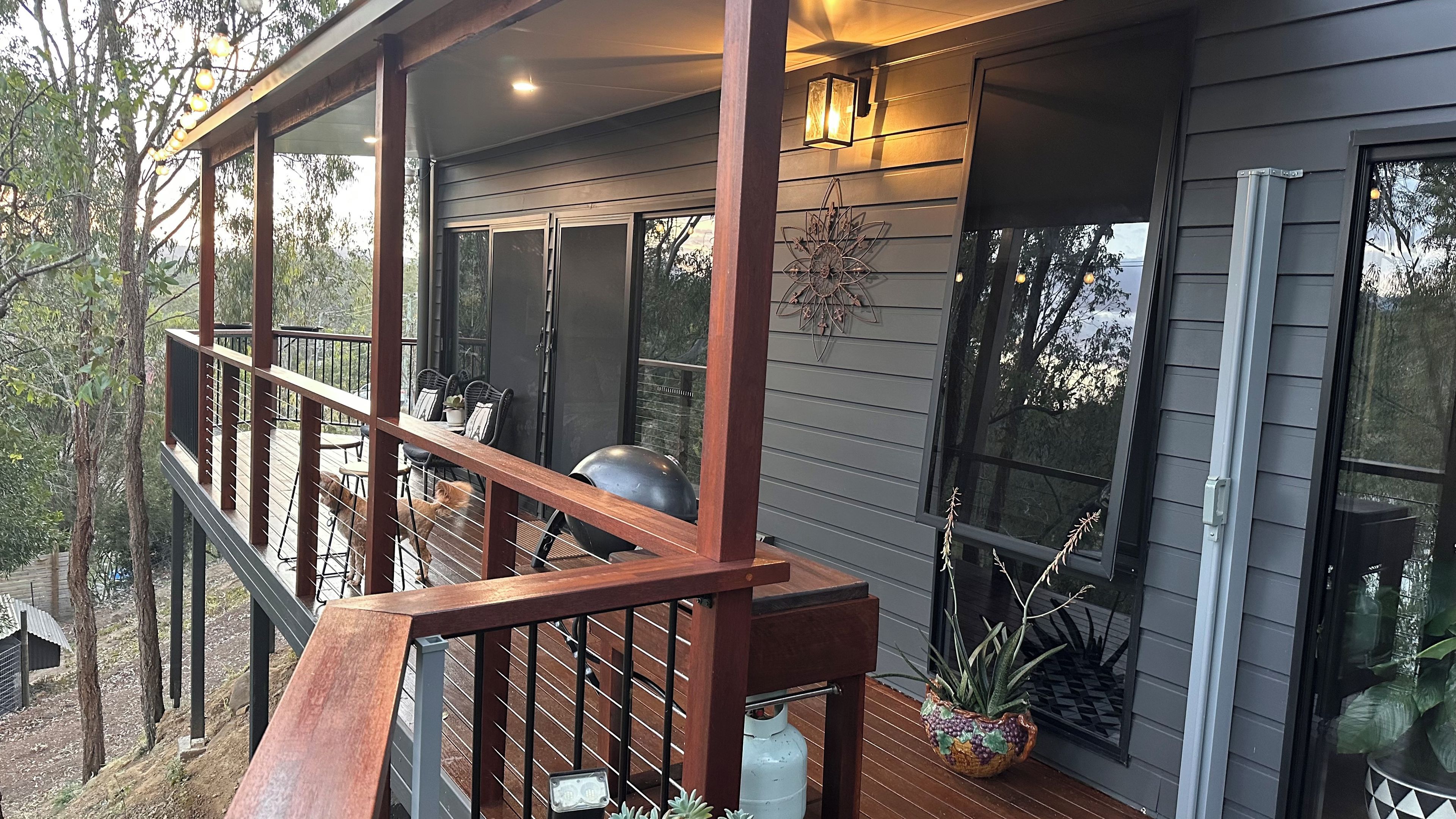 A covered outdoor deck with a railing, a gas tank, and potted plants.