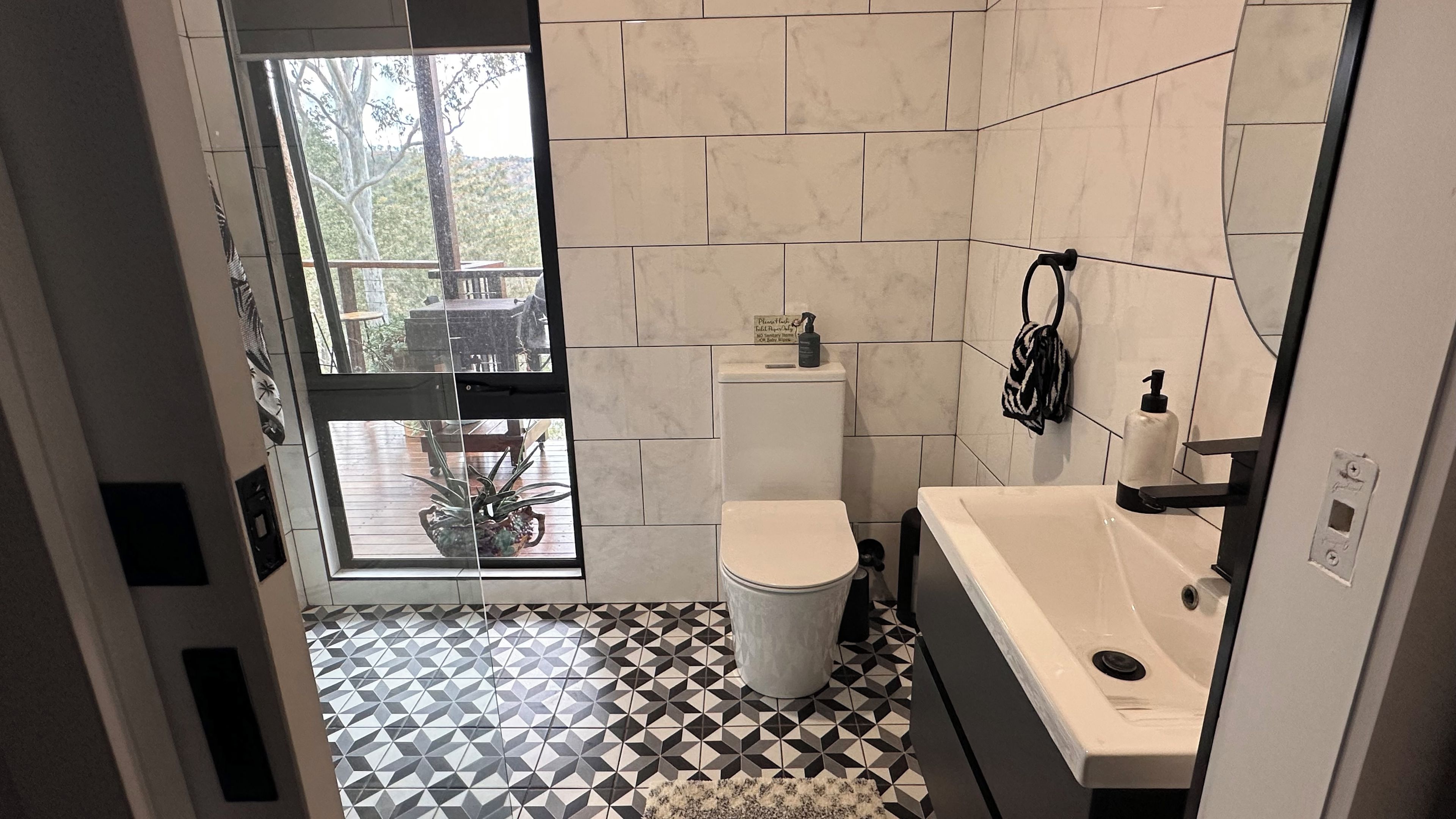 Ein Badezimmer mit Toilette, Waschbecken und Blick ins Freie durch eine Glastür.