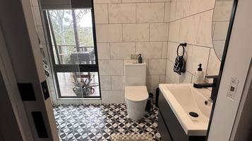 Ein Badezimmer mit Toilette, Waschbecken und Blick ins Freie durch eine Glastür.