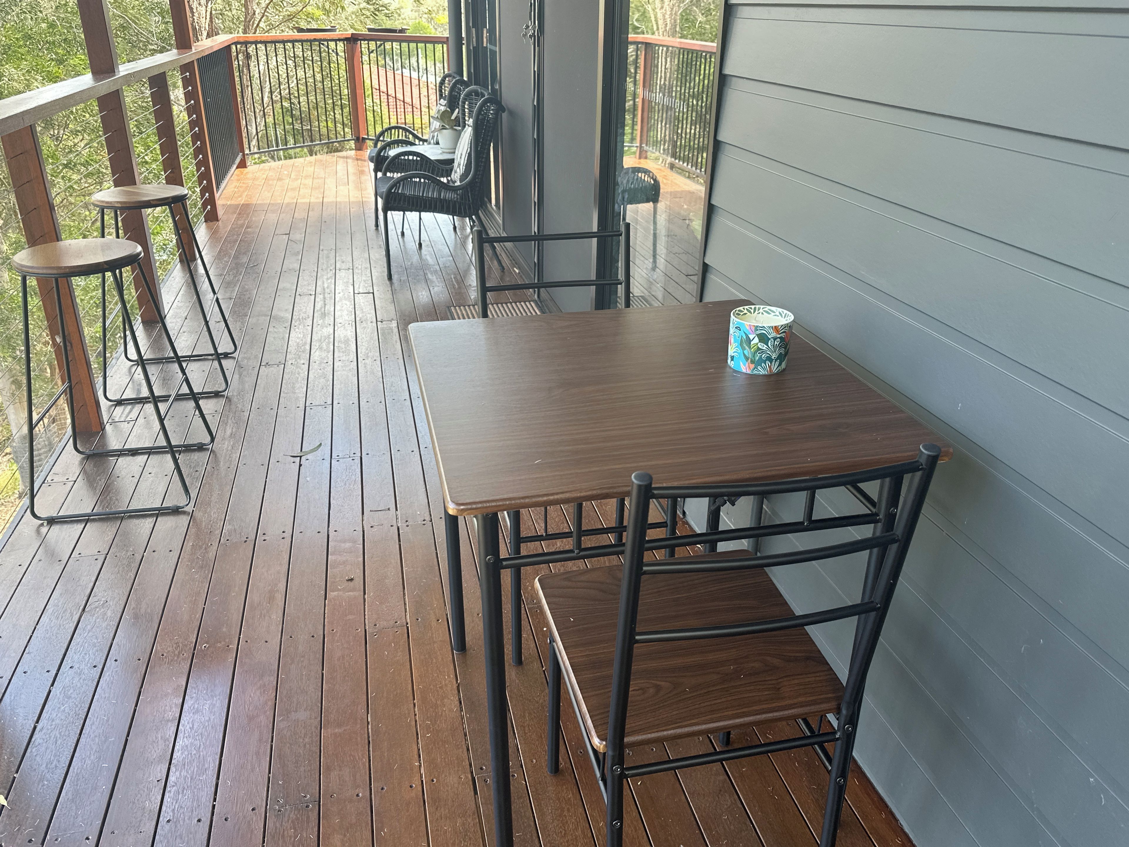 A wooden deck with a table and chairs, a railing, and a view of the outdoors.